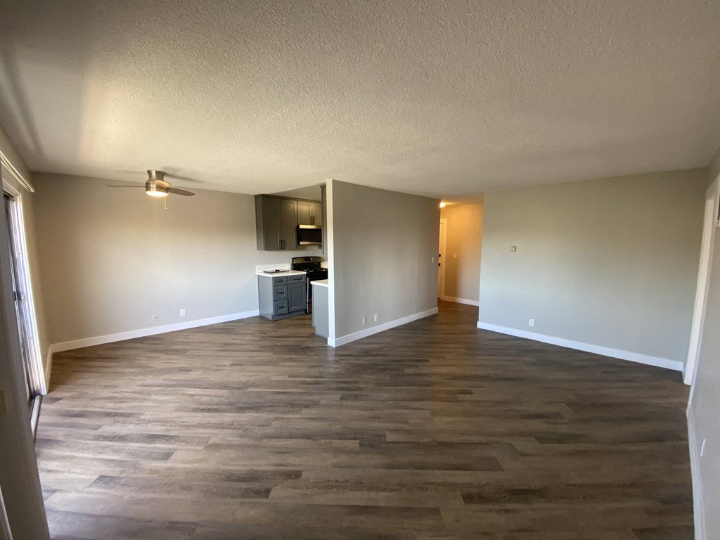 an empty living room with wooden floors and a kitchen