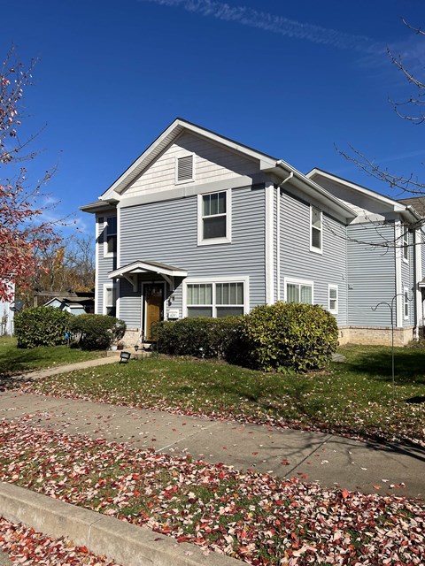 A grey house with a yellow door and a green bush in front.