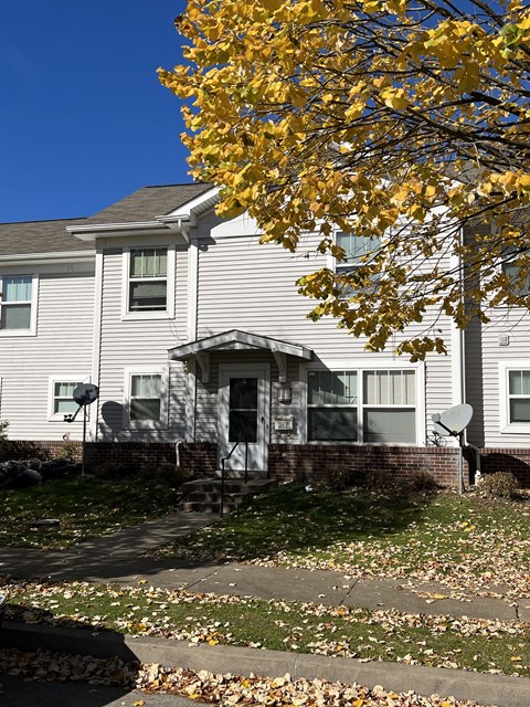 A house with a grey facade and a tree with yellow leaves in front.