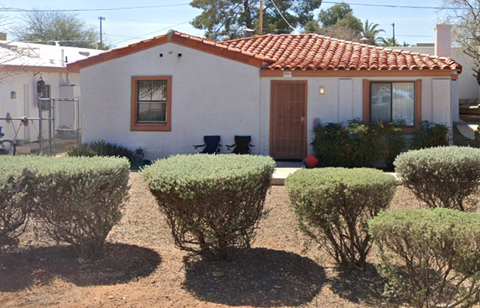 A small white house with a red tile roof and a brown door.