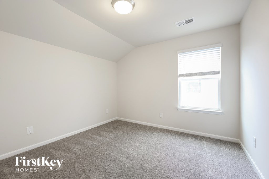 A carpeted room with a window and a light on the ceiling.
