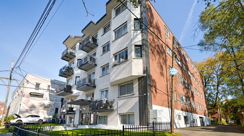 A multi-story building with a mix of white and brick facades, featuring balconies and windows.