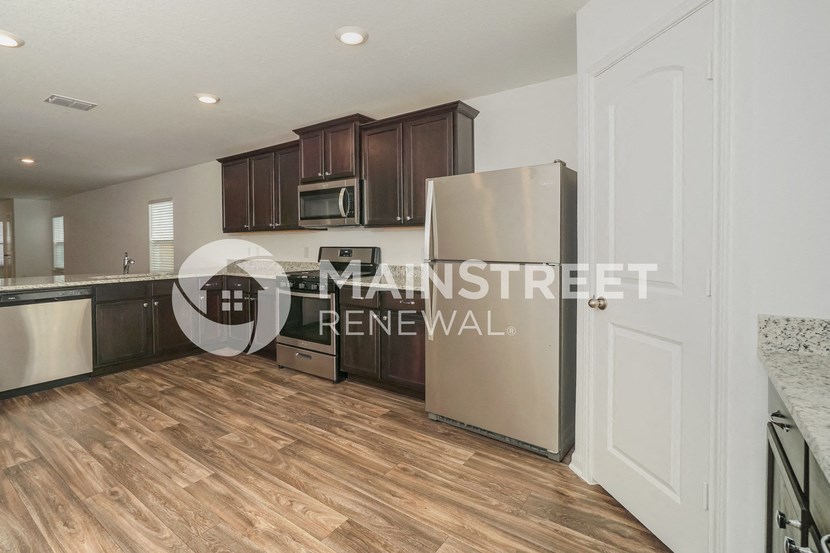 a kitchen with wooden floors and cabinets and a stainless steel refrigerator