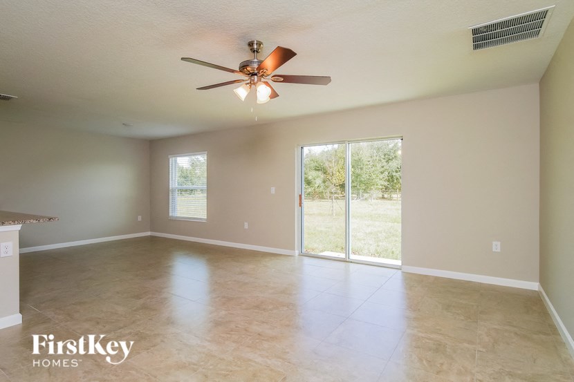 A spacious room with a ceiling fan and sliding glass doors leading to a backyard.
