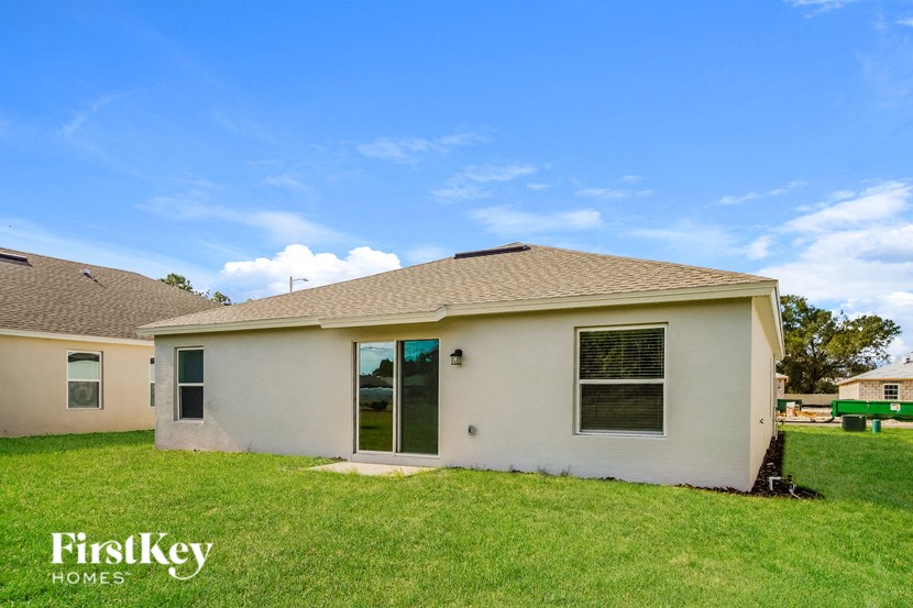 A small house with a brown roof and a white exterior is surrounded by a grassy lawn.