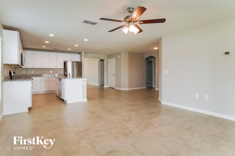 A spacious kitchen and living room with a ceiling fan and lighting fixtures.