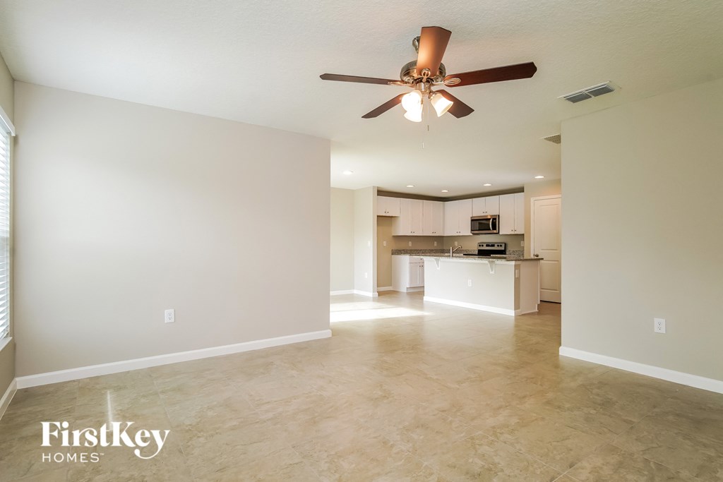 an empty living room with a ceiling fan and a kitchen
