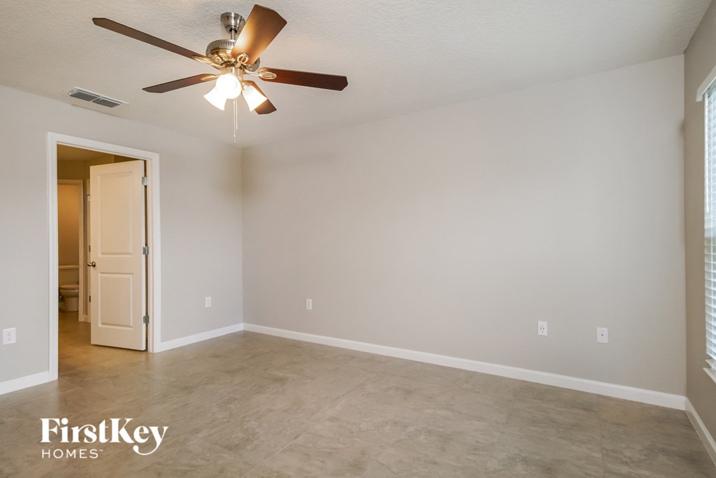 a empty living room with a ceiling fan and a door to a hallway