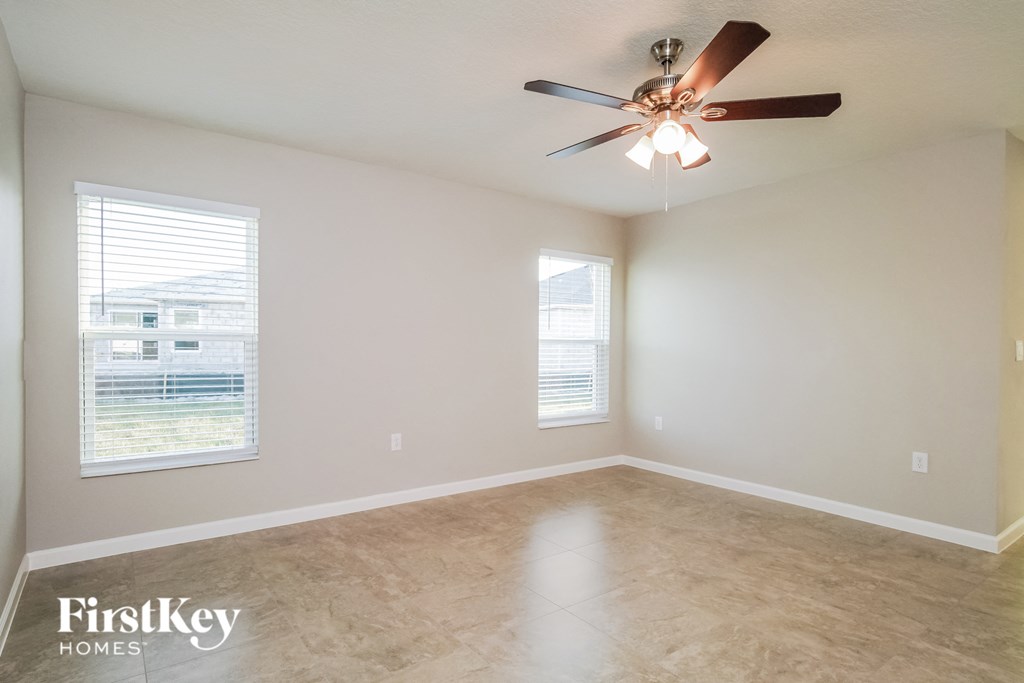 an empty living room with a ceiling fan and two windows