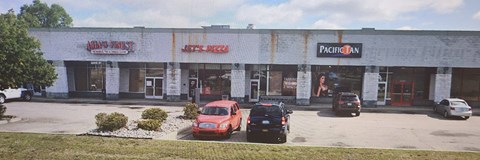 A red car is parked in front of a building with a sign that says "Jet's Pizza".