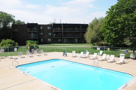 A large swimming pool surrounded by chairs and apartment buildings.