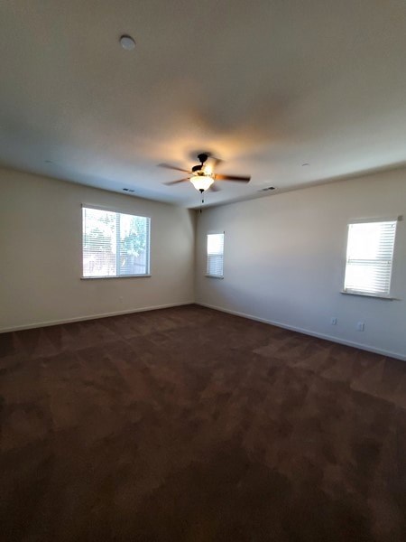 A room with a ceiling fan and two windows.