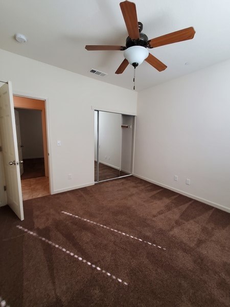 A room with a ceiling fan and brown carpet.