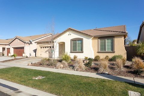 A house with a brown roof and tan walls with a green lawn in front.