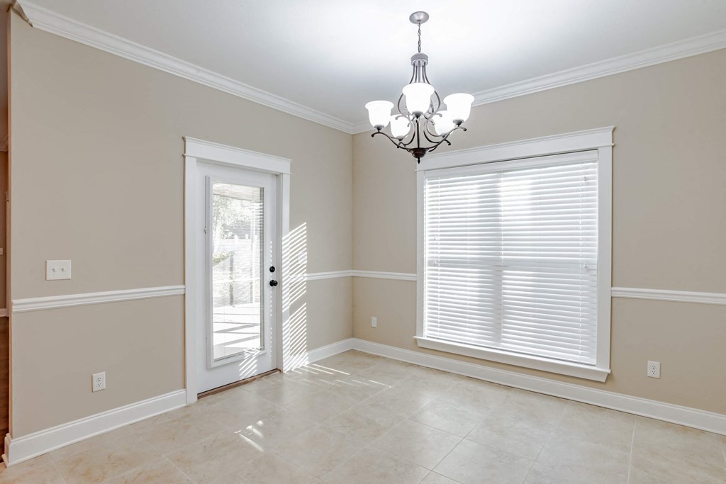 A room with a chandelier, a window with blinds, and a door leading to a patio.