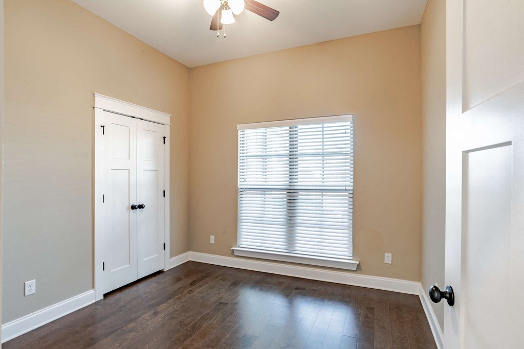 A room with a door, a window with blinds, and a ceiling fan.