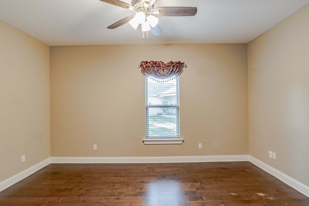 A room with a ceiling fan and a window with a red curtain.