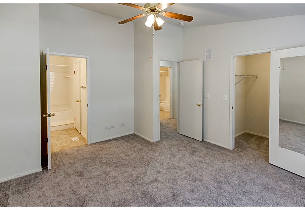 an empty bedroom with a ceiling fan and three closets