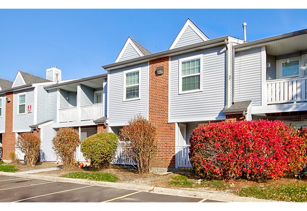 an apartment building with white siding and red bushes