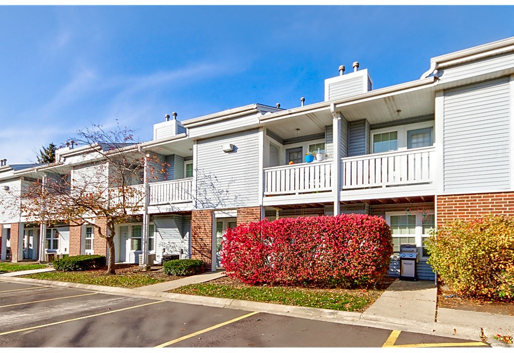 an apartment building with balconies and a red bush in front