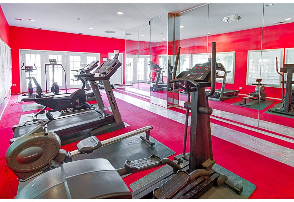 a gym with cardio equipment and mirrors in a red room