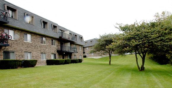 an apartment building with a green lawn and trees