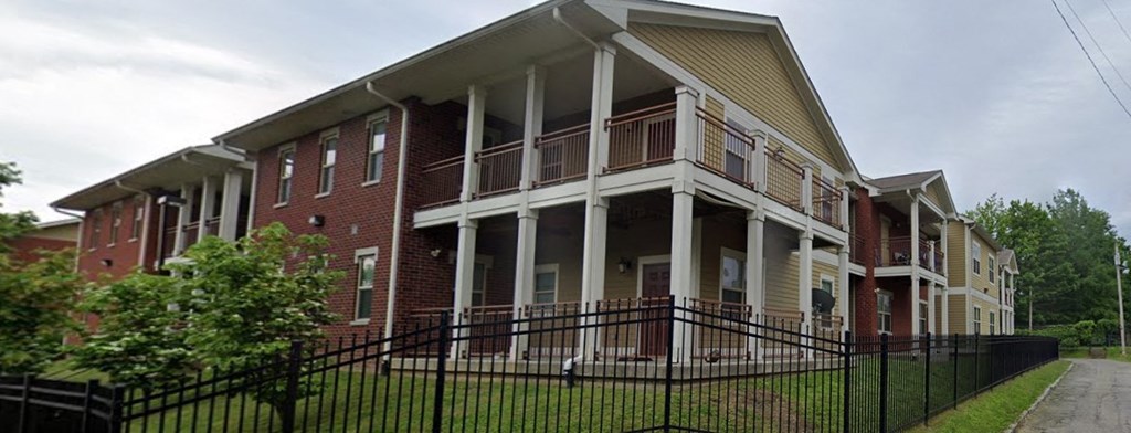 a red brick house with white columns and a black fence