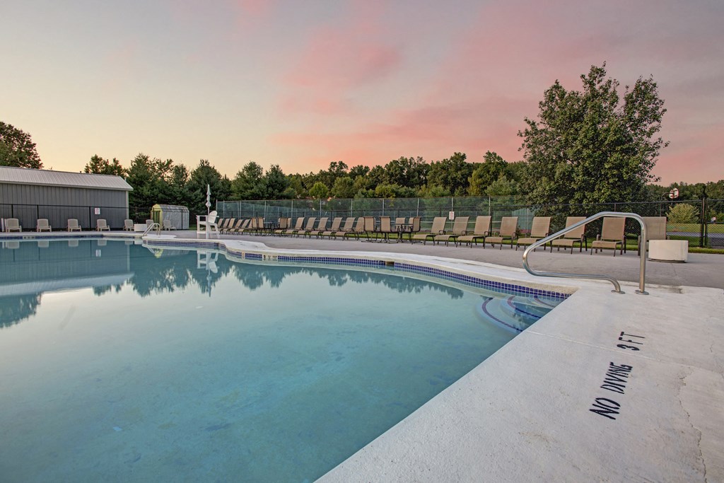 a swimming pool with chairs around it at sunset