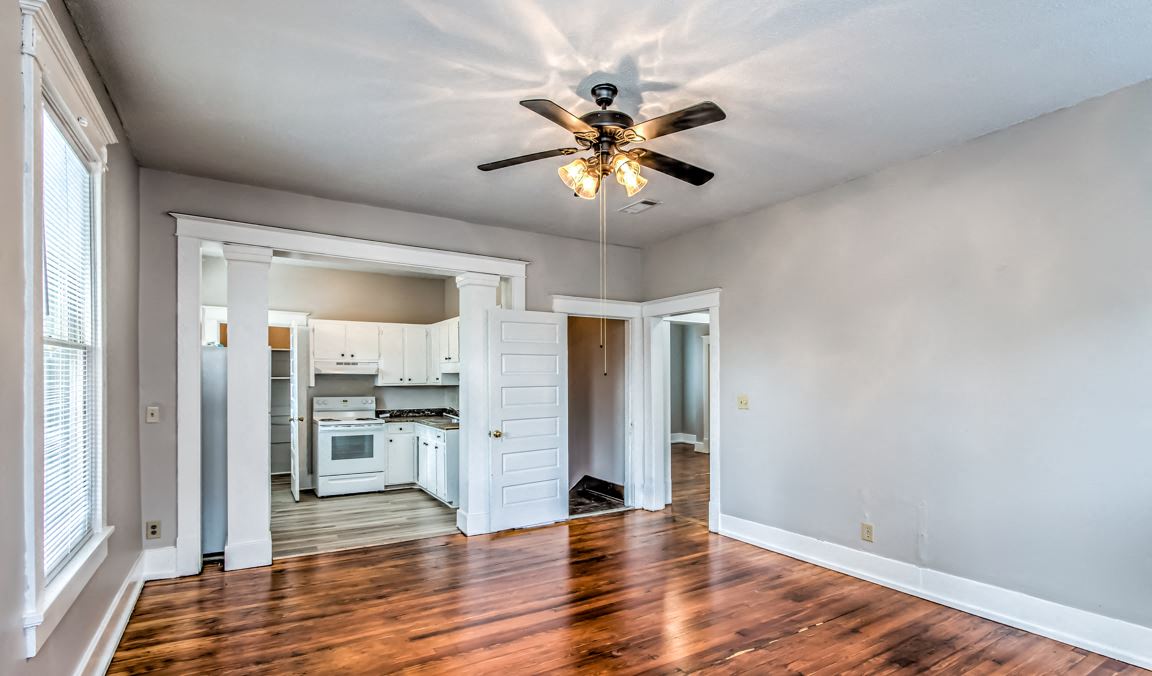 an empty living room with a ceiling fan and a kitchen