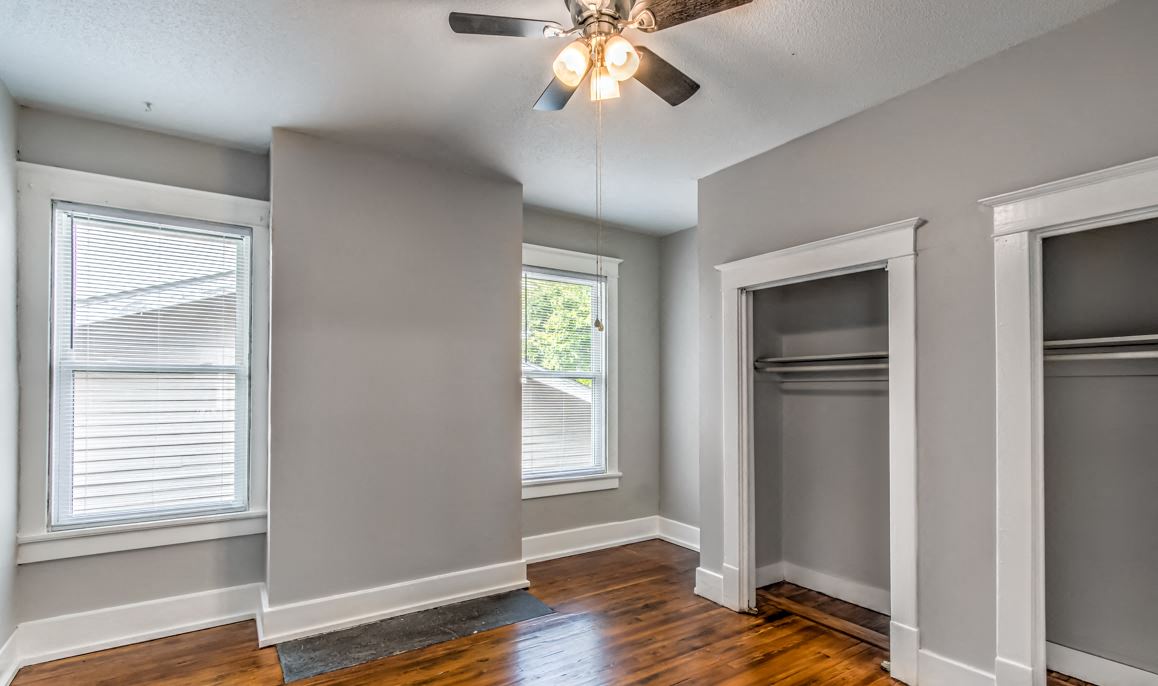 an empty room with two windows and a ceiling fan