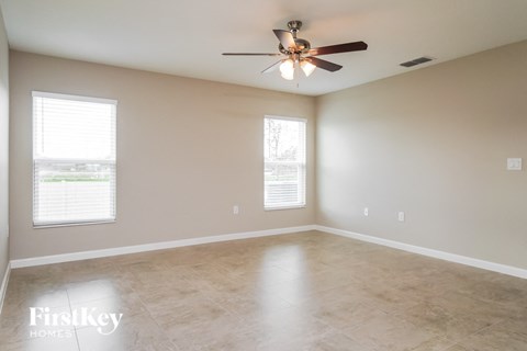 A spacious room with a ceiling fan and two windows.