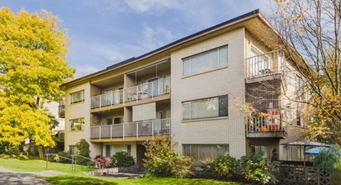 Apartment building with balconies and trees in front.
