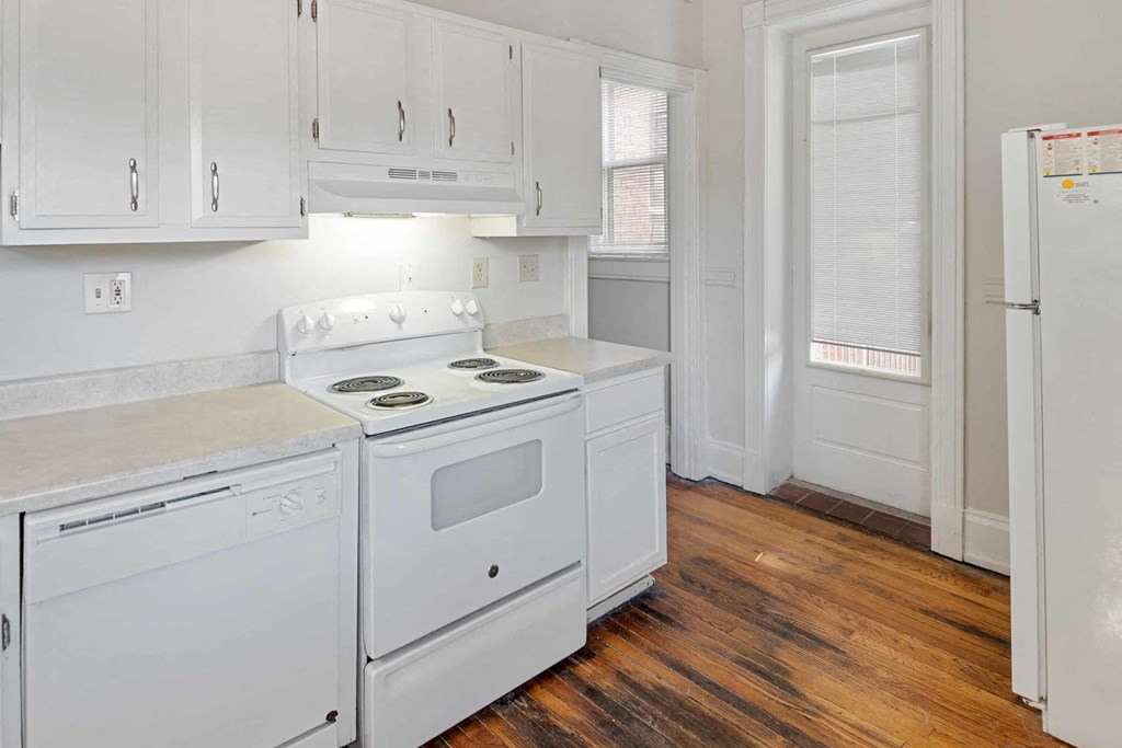 A white kitchen with a white fridge and white cabinets.