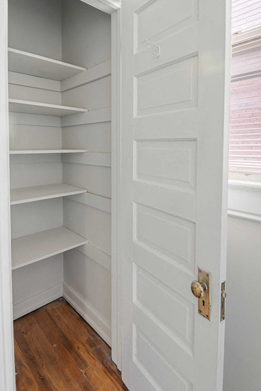 A white door with a brass handle is open to a pantry with shelves.