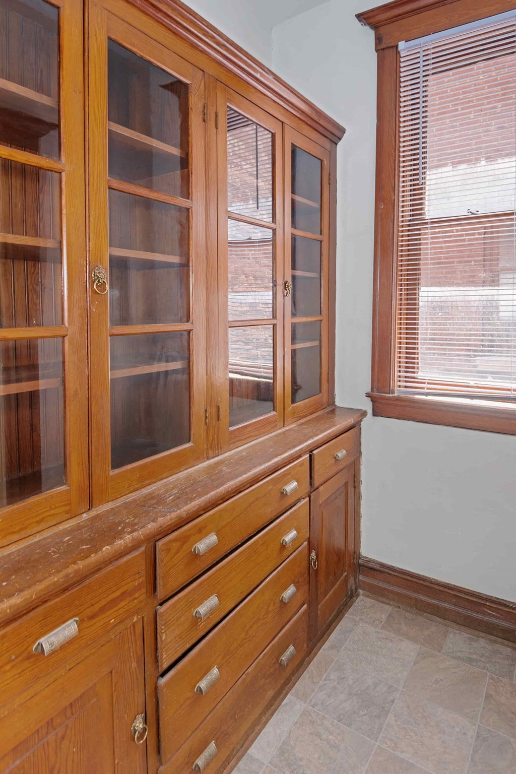 A wooden cabinet with glass doors and drawers is in a room.