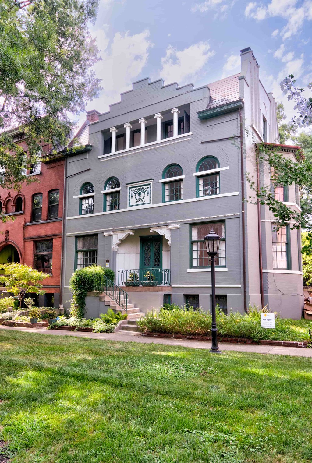 A grey building with green shutters and a white sign in front.