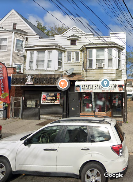 A white car is parked in front of a Zapata Barbershop.