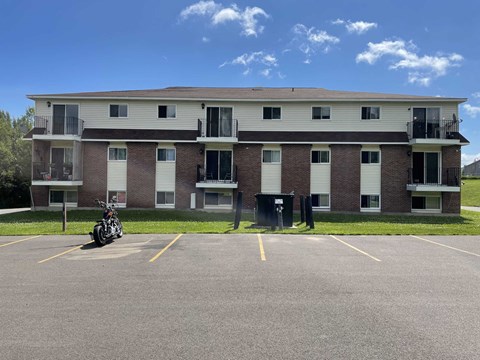 A motorcycle is parked in a parking lot in front of a brick apartment building.