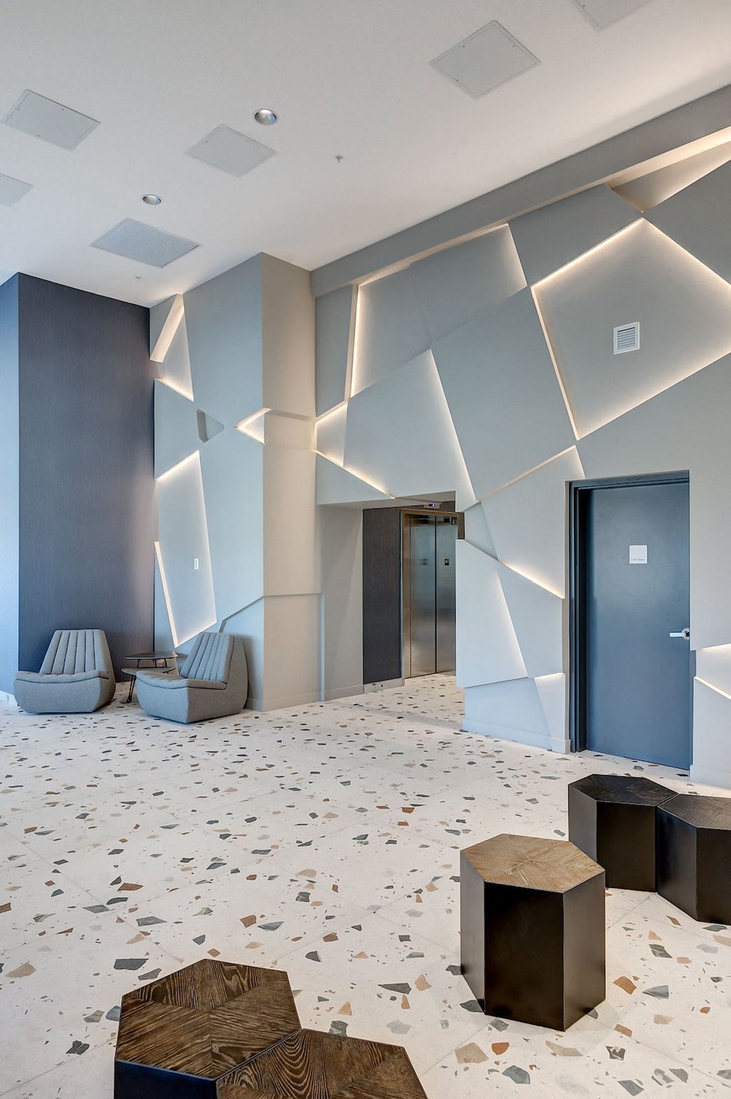 a lobby with a blue door and a marble floor with seats and cubes