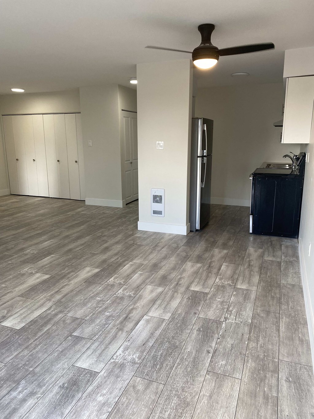 an empty living room with wood floors and a refrigerator