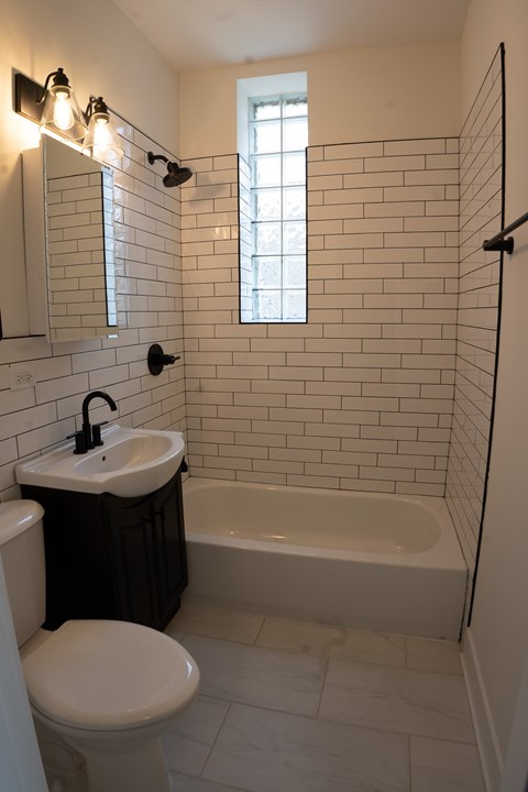A white toilet sits next to a sink in a bathroom with a black trash can.