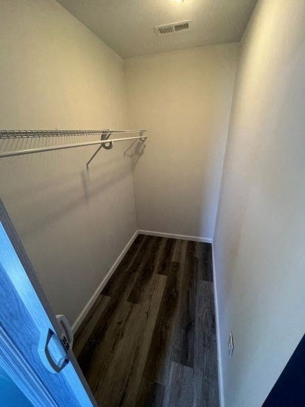 A walk in closet with a white wall and a wooden floor.