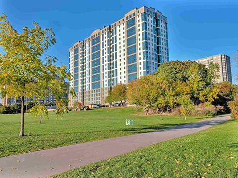 A tall building with many windows is surrounded by trees and a grassy area.