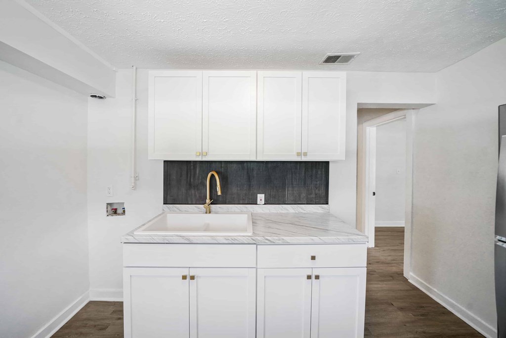a white kitchen with white cabinets and a sink and a gold faucet