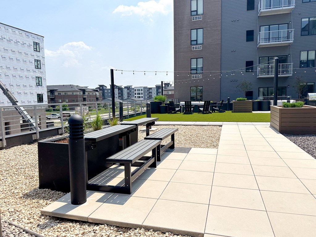 a roof top patio with benches and a grassy area with buildings in the background