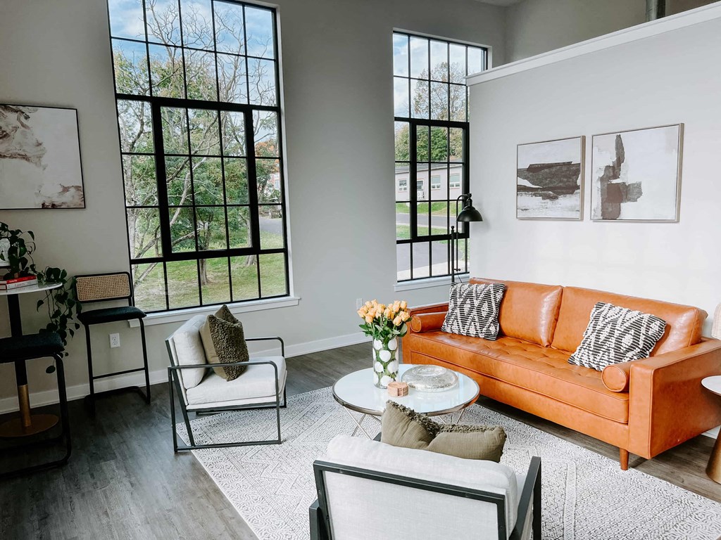 a living room with a orange couch and chairs and large windows