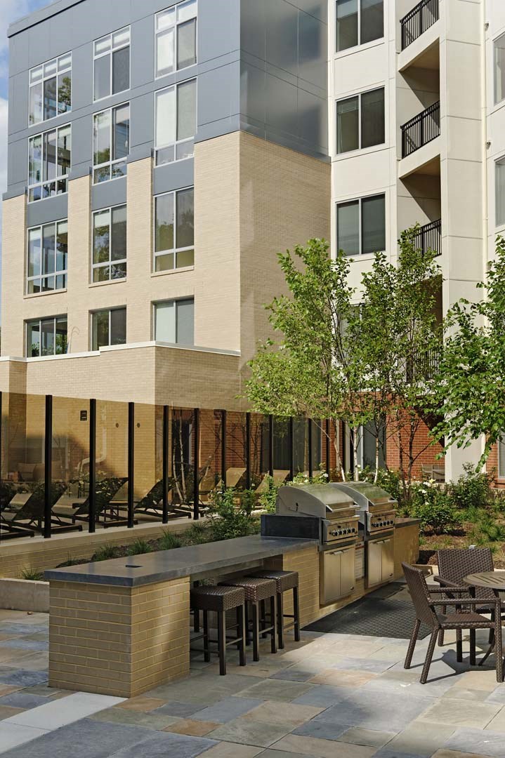 a patio with a grill and tables in front of an apartment building