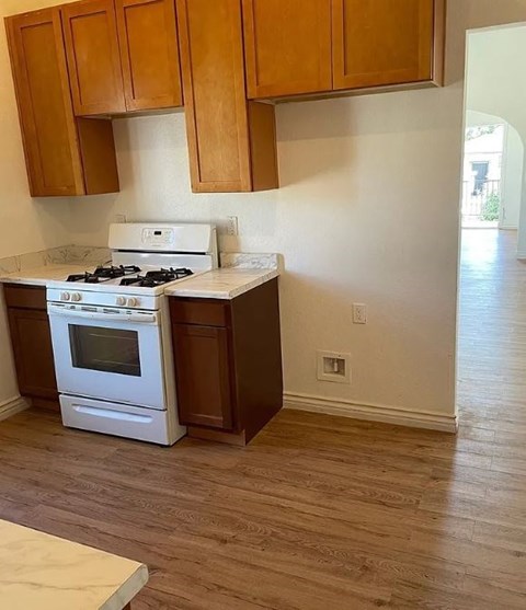 A kitchen with a white stove and oven, wooden cabinets, and a wooden floor.