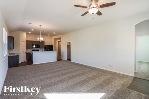 A spacious living room with a carpeted floor and a ceiling fan.