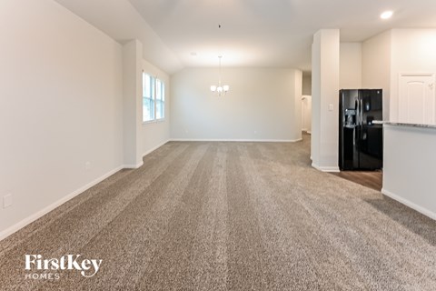 A spacious, empty room with a carpeted floor and a black refrigerator in the corner.